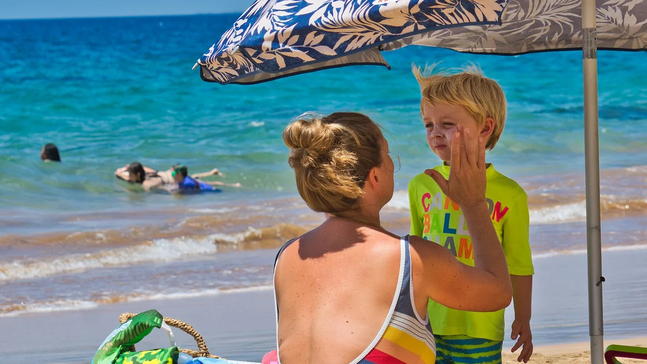Aplicação de protetor solar no rosto de uma criança na praia