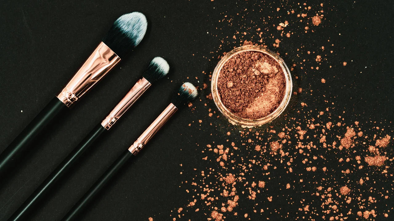 Três pincéis ao lado de um bronzer em pó espalhado, em imagem ilustrativa
