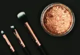 Bronzer em pó e pincéis de maquiagem sobre fundo escuro, em imagem ilustrativa