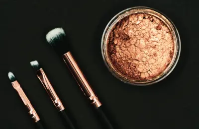 Bronzer em pó e pincéis de maquiagem sobre fundo escuro, em imagem ilustrativa
