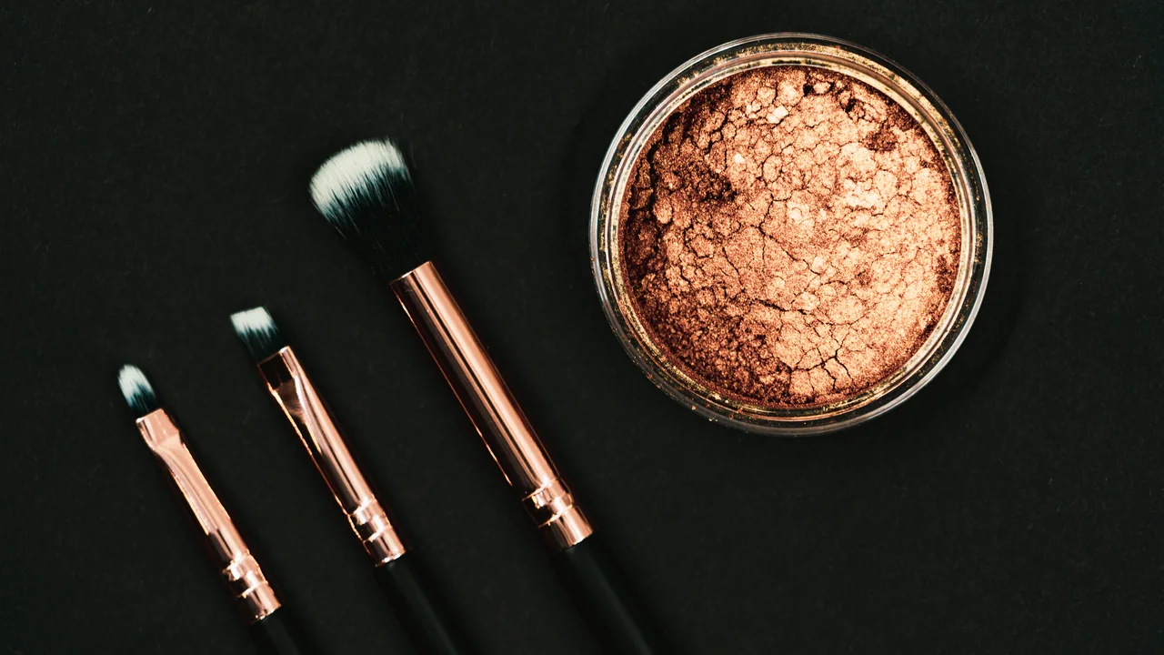Bronzer em pó e pincéis de maquiagem sobre fundo escuro, em imagem ilustrativa