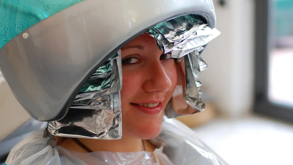 Pessoa com mechas de cabelo envoltas em papel-alumínio sob um secador de salão
