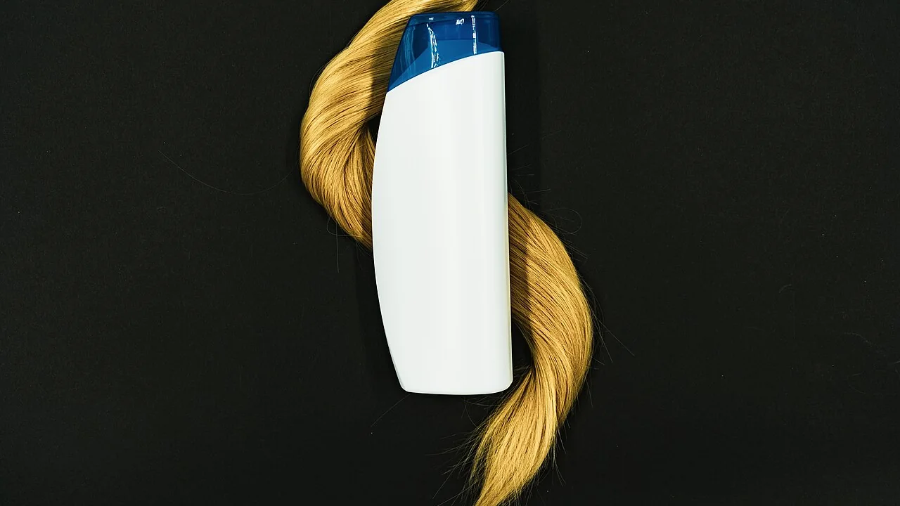Frasco ilustrativo de condicionador junto a uma mecha de cabelo