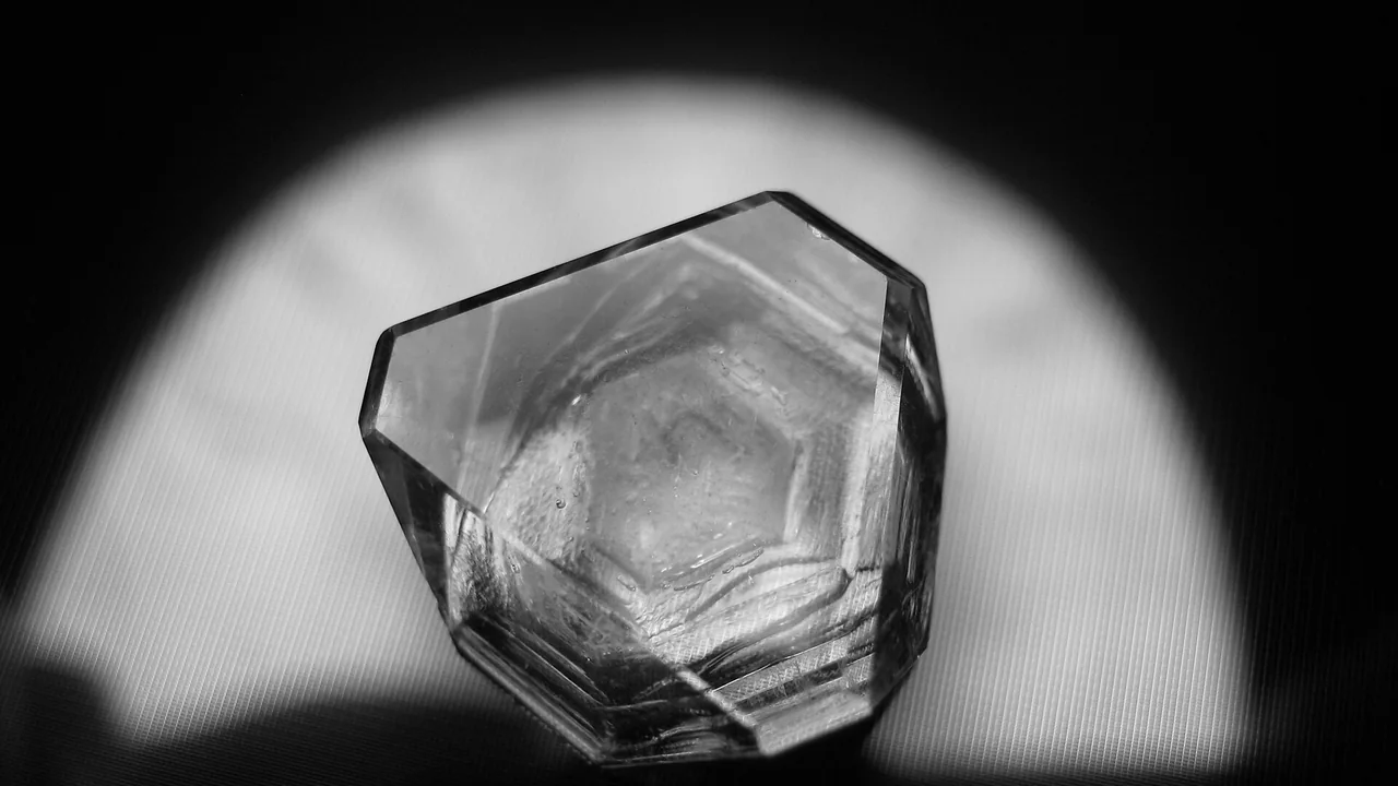 Cristal octaédrico de alúmen em fotografia monocromática; imagem ilustrativa da matéria-prima, não de uma embalagem comercial.