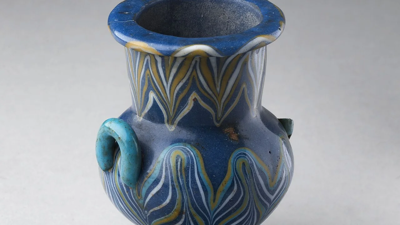 Detalhe de recipiente cosmético histórico de vidro com decoração azul e dourada, usado como ilustração.