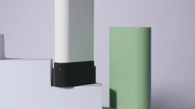 Embalagem oval em bastão para perfume sólido, apresentada fechada em verde e aberta em branco