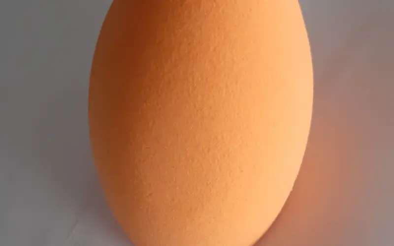 Esponja de maquiagem laranja seca em close sobre uma superfície neutra