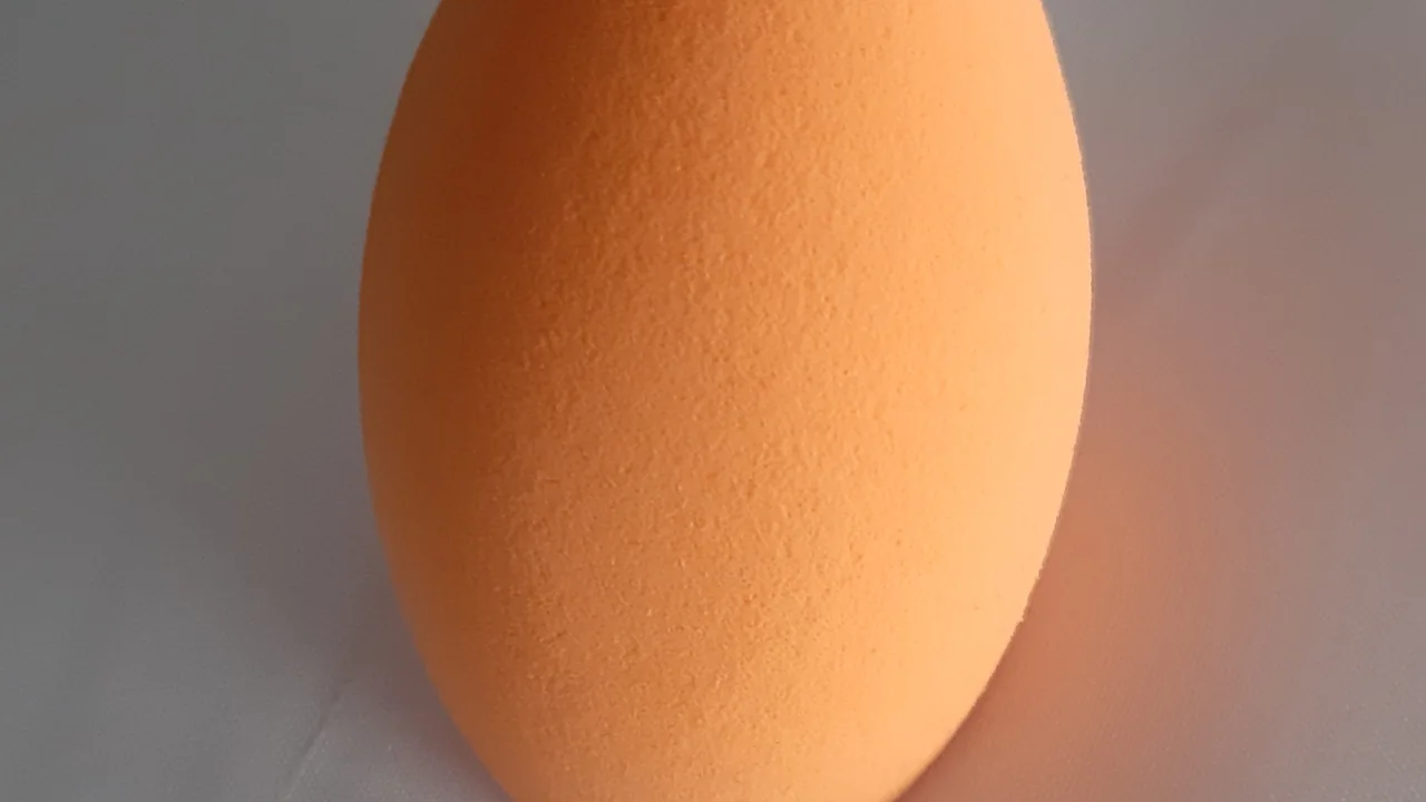 Esponja de maquiagem laranja seca em close sobre uma superfície neutra