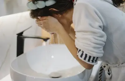 Pessoa lavando o rosto com água em uma pia