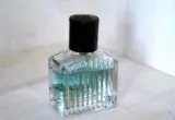 Frasco de perfume de vidro com líquido azul-claro e tampa preta sobre uma superfície clara