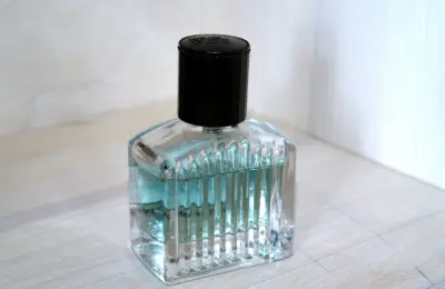 Frasco de perfume de vidro com líquido azul-claro e tampa preta sobre uma superfície clara