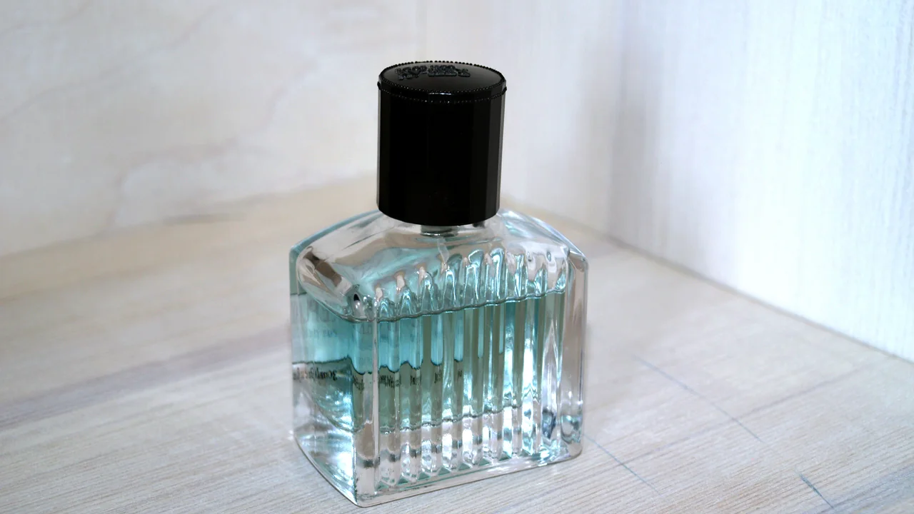 Frasco de perfume de vidro com líquido azul-claro e tampa preta sobre uma superfície clara