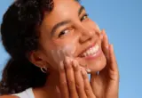 Pessoa aplicando produto de limpeza ou esfoliação facial com movimentos suaves no rosto.