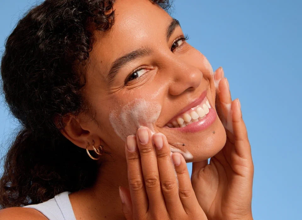 Pessoa aplicando produto de limpeza ou esfoliação facial com movimentos suaves no rosto