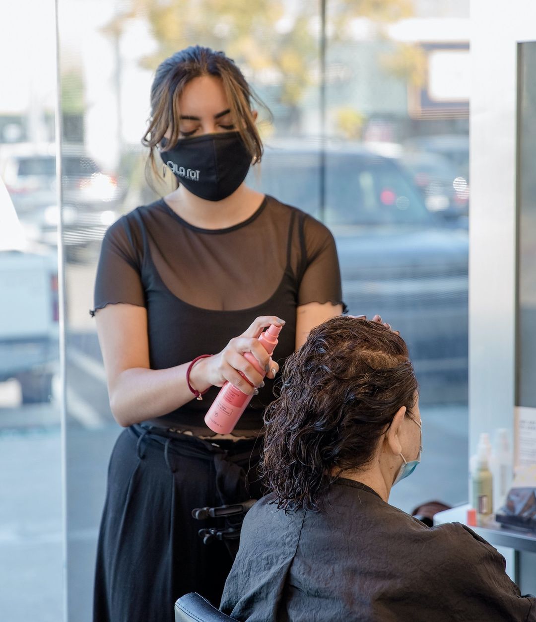 Profissional aplica spray de finalização no cabelo de uma cliente em salão