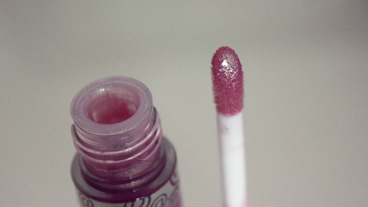 Aplicador de gloss labial ao lado do frasco aberto em imagem ilustrativa