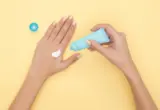 Pessoa aplicando creme nas mãos em fundo amarelo
