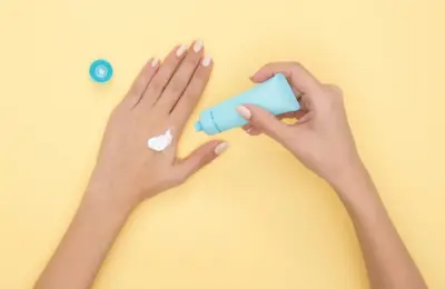 Pessoa aplicando creme nas mãos em fundo amarelo