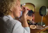 Espelho de mesa refletindo uma pessoa enquanto aplica maquiagem; imagem ilustrativa.