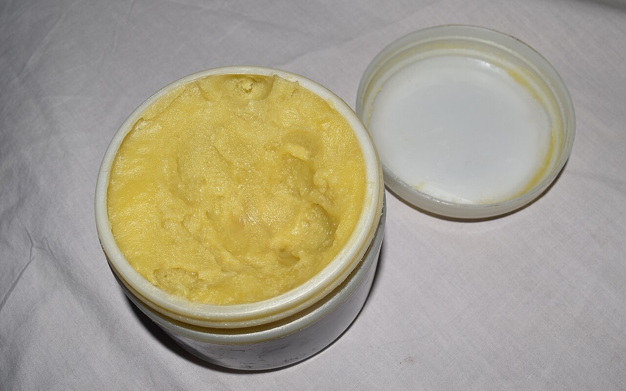 Pote aberto com manteiga de karité usada como base para produto de massagem