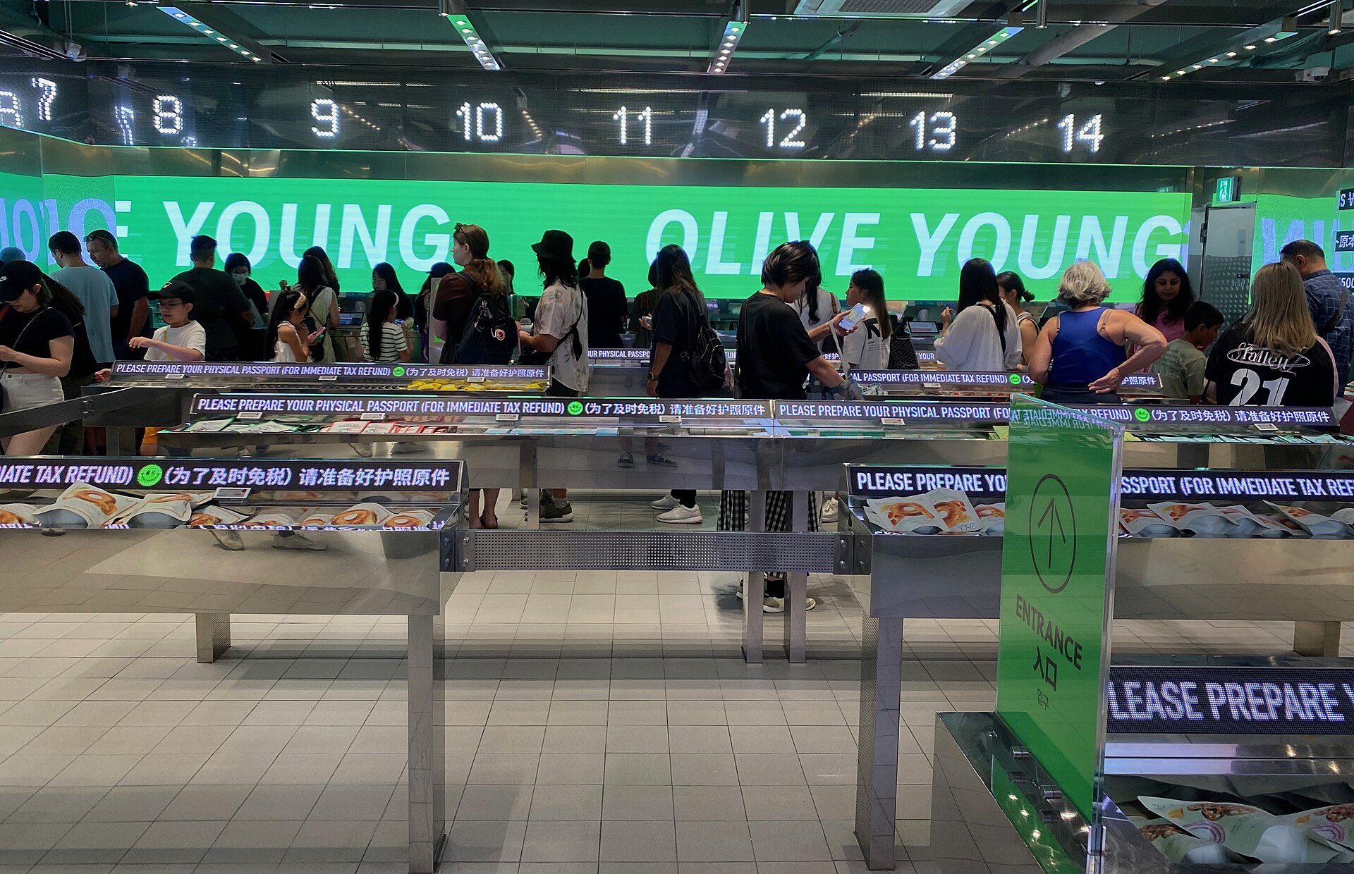 Interior de uma loja Olive Young em Myeongdong, Seul, com o logotipo verde da rede e clientes diante dos caixas
