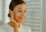 Mulher sorrindo toca o rosto em uma cena de cuidados com a pele madura