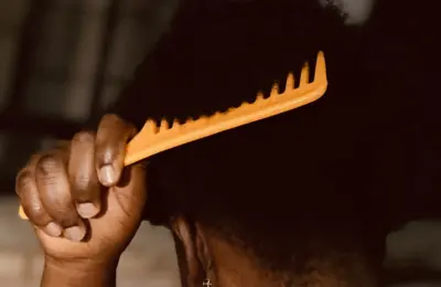 Pente de dentes largos sendo usado em cabelo crespo; imagem ilustrativa.