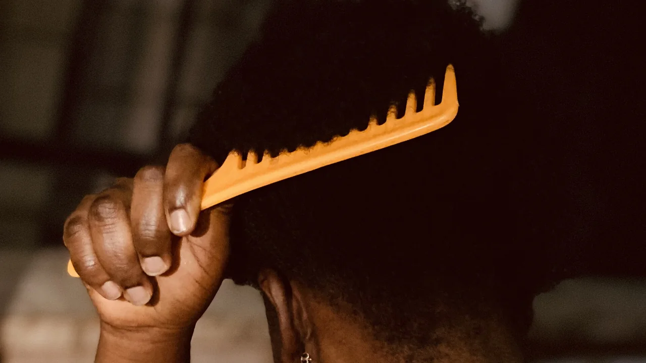Pente de dentes largos sendo usado em cabelo crespo; imagem ilustrativa.