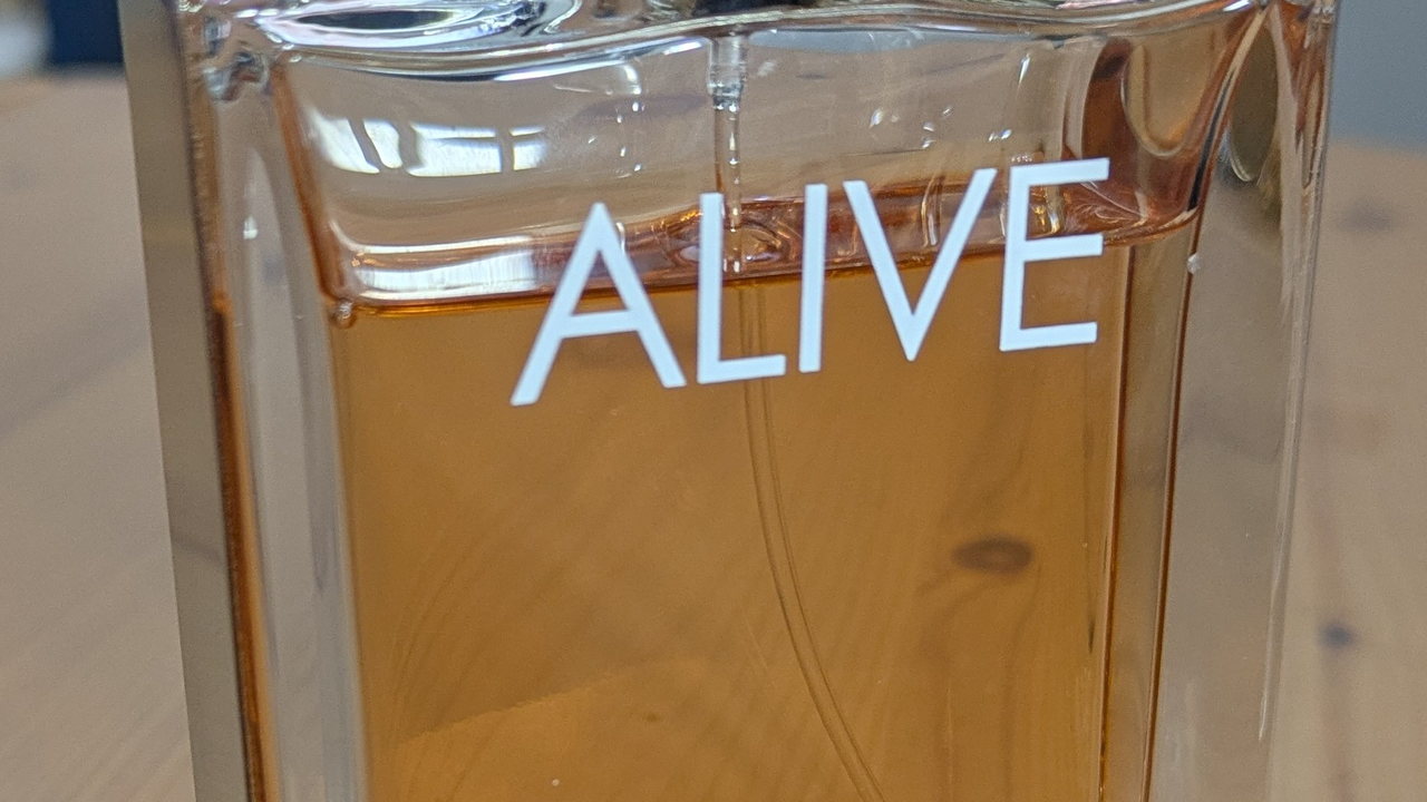 Detalhe de uma garrafa de perfume Alive com líquido âmbar