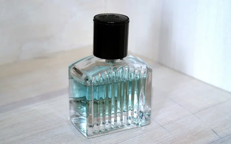 Frasco de perfume transparente com tampa preta sobre superfície clara, imagem ilustrativa