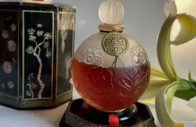 Garrafa vintage de perfume Suma ao lado da caixa decorada e de uma flor