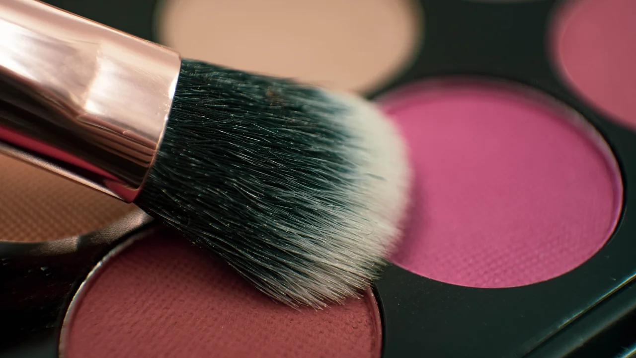 Pincel de maquiagem sobre uma paleta de sombras, em close, destacando o formato das cerdas.