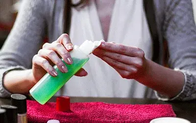 Mãos seguram algodão e frasco de removedor durante a preparação para remover esmalte em gel