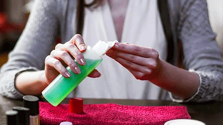 Mãos seguram algodão e frasco de removedor durante a preparação para remover esmalte em gel
