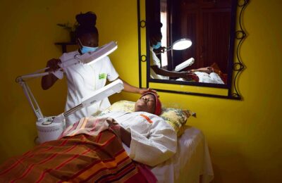 Profissional realizando atendimento facial com lupa e iluminação sobre cliente