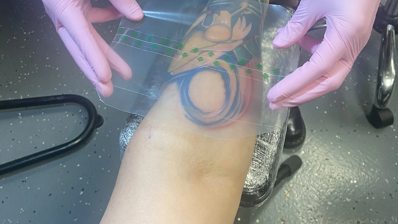 Tatuagem recém-feita coberta por película protetora durante a fase inicial de cuidado.