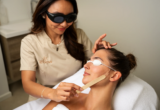 Profissional realiza procedimento facial em cliente sobre maca de estética.