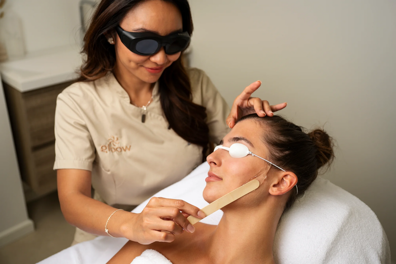 Profissional realiza procedimento facial em cliente sobre maca de estética.