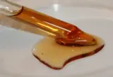 Imagem ilustrativa de um sérum oleoso com vitamina E e creme cosmético em uma placa branca