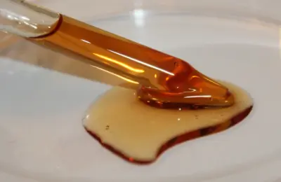 Imagem ilustrativa de um sérum oleoso com vitamina E e creme cosmético em uma placa branca