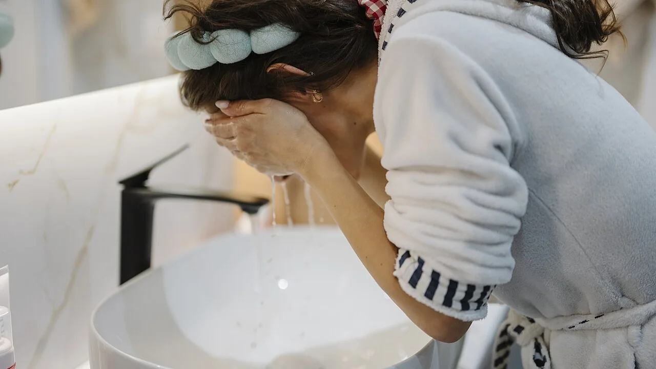 Mulher lavando o rosto em uma pia, imagem contextual para explicar a etapa de limpeza facial