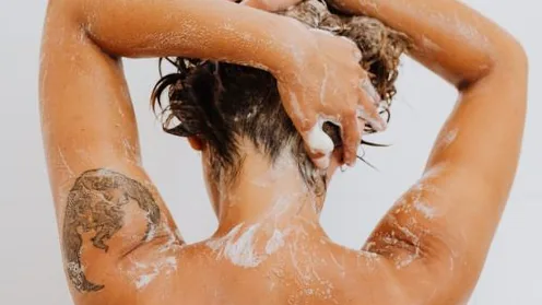 Pessoa lavando o cabelo com espuma no chuveiro
