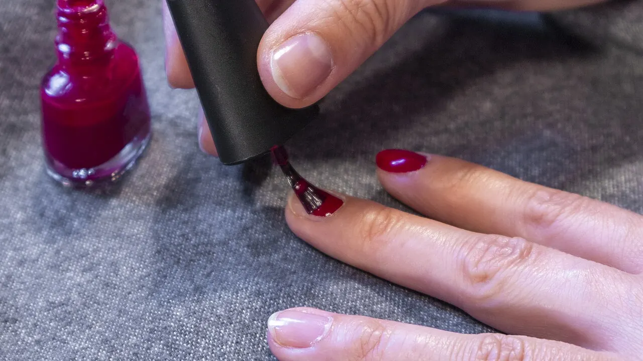 Pessoa aplicando esmalte vermelho em uma unha