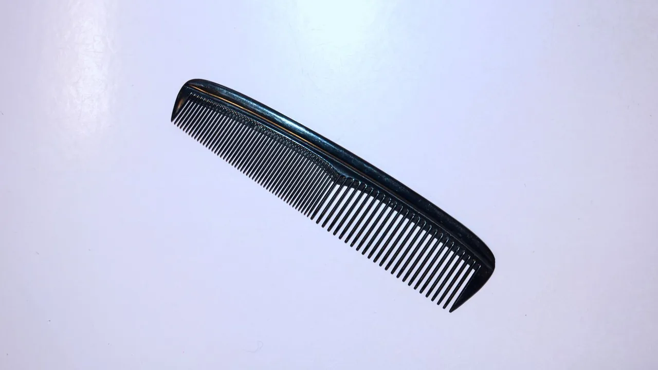 Pente preto de dentes finos sobre fundo claro.