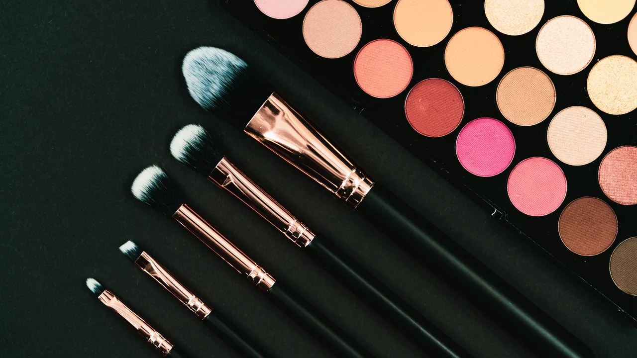 Paleta de sombras coloridas e pincéis de maquiagem sobre fundo escuro.