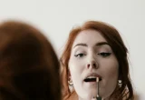 Pessoa aplicando produto de maquiagem nos lábios diante do espelho