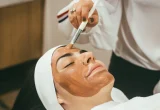 Profissional aplica máscara de skincare no rosto de uma mulher