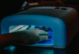 Mão com unhas em gel sob uma cabine de luz LED