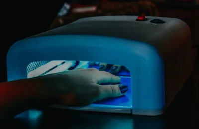 Mão com unhas em gel sob uma cabine de luz LED