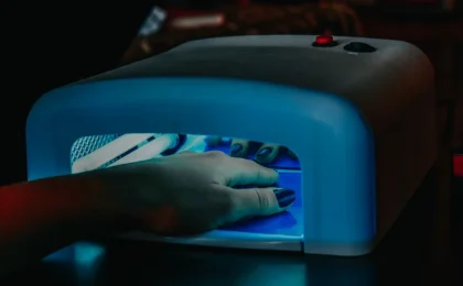 Mão com unhas em gel sob uma cabine de luz LED